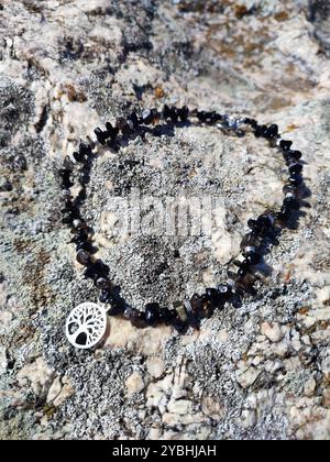 Schwarzer Obsidian Choker mit Baum des Lebens Anhänger an grauer Granitfelsenoberfläche | Chunky Halskette aus Naturstein mit Baum des Lebens Charme Stockfoto