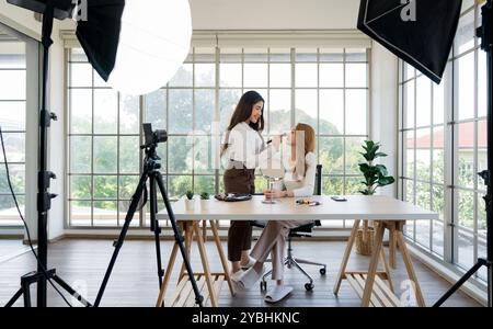 Zwei asiatische Frauen, die Inhalte für soziale Medien erstellen. Sie verwenden eine Studioeinrichtung, die eine auf einem Stativ montierte Kamera, Beleuchtungsausrüstung und einen VAR umfasst Stockfoto