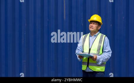 Leitender Transportarbeiter in Sicherheitsweste und gelbem Schutzhelm mit Dokumentenablage vor einem großen Frachtcontainer stehen. Stockfoto