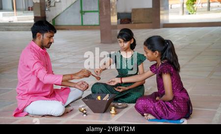 Eine indische Familie in traditioneller Kleidung führt eine Yagya oder Havan aus, die von einem Priester geleitet wird, um die Energien in ihrem Haus auszugleichen. Dieser heilige pooja ist für Harmonie Stockfoto