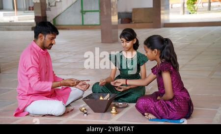 Eine indische Familie in traditioneller Kleidung führt eine Yagya oder Havan aus, die von einem Priester geleitet wird, um die Energien in ihrem Haus auszugleichen. Dieser heilige pooja ist für Harmonie Stockfoto