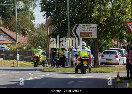 An einer unangenehmen, versetzten Straßenkreuzung der Tour of Britain 2024 halten zwei Motorradfahrer der Polizei an einem großen Straßenschild, das nach links nach Badingham zeigt. Stockfoto