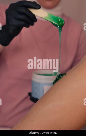 Wachssitzung in einem Schönheitssalon mit grünem Wachs, das während der Behandlung auf die Haut aufgetragen wird Stockfoto