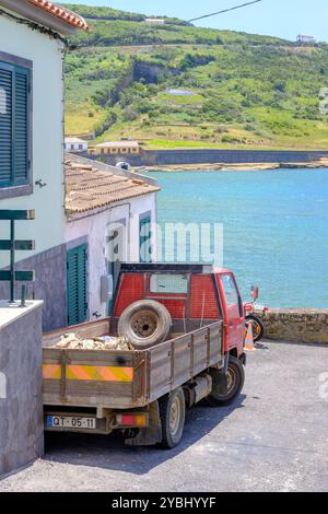 Ein alter roter Truck parkt neben einem Haus in Faial, Horta, Azoren, mit Blick auf das blaue Wasser des Atlantischen Ozeans. Die malerische Landschaft bietet sich an Stockfoto