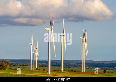 Windturbinen stehen hoch auf einem Feld und ihre Rotorblätter drehen sich sanft gegen die orange- und rosa Farbtöne des Sonnenuntergangs. Die ruhige Landschaft verbindet erneuerbare Energien Stockfoto