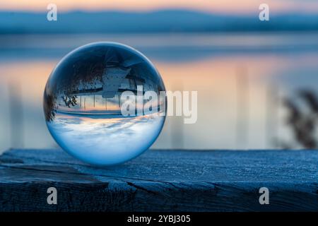 Eine Glaskugel sitzt auf einer Holzoberfläche und reflektiert den Himmel und das Wasser. Das Konzept der Ruhe und Ruhe, wie die Reflexion des Balls einfängt Stockfoto