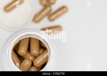 Pflanzliche Arzneimittelkapseln, die aus einer offenen Flasche auf einem weißen Hintergrund verschüttet werden Stockfoto