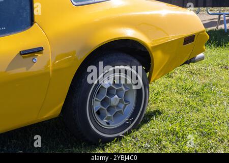 Nahaufnahme des Hinterrads eines gelben pontiac Feuervogels Trans am, der auf einem grasbewachsenen Feld geparkt ist Stockfoto