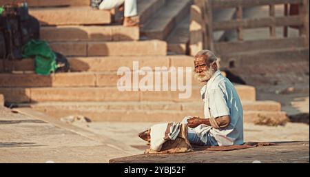 Varanasi, Indien. Der Alte Bettler Zählt Seine Einnahmen. Ein Alter Mann Sitzt Am Ganges Embankment. Der Senior-Mann Zählt Sein Geld. Vormittag Im Heiligen Varanasi Ghats Stockfoto