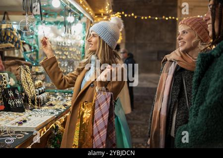 Zwei junge Frauen, die Schmuck auf einem Weihnachtsmarkt suchen. Freunde, die gerne im Urlaub einkaufen, umgeben von festlichen Lichtern und Dekorationen. Winter Stockfoto