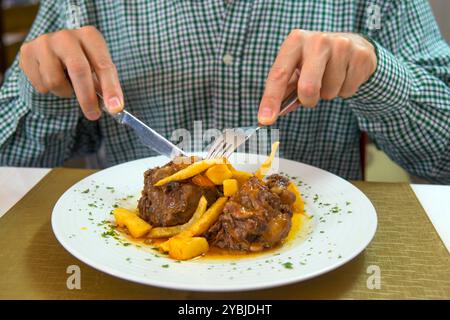 Männerhände schneiden Rabo de toro, ein typisches spanisches Fleischgericht. Ansicht schließen. Stockfoto