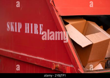 Ein Red Hired Skip oder Müllcontainer gefüllt mit Kartonschachteln Stockfoto