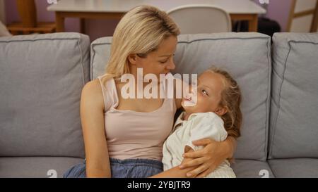 Kaukasische Mutter und Tochter verbringen einen liebevollen Moment zusammen auf einer bequemen Couch in ihrem gemütlichen Wohnzimmer. Stockfoto