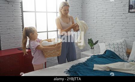 Frau und Kind zusammen machen zu Hause ein Bett im Schlafzimmer, falten Wäsche mit einem Korb auf dem Bett. Stockfoto