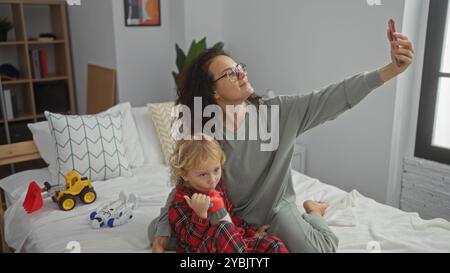 Frau macht Selfie mit Sohn im gemütlichen Schlafzimmer, hält liebevolle Familienmomente drinnen fest, zeigt Mutter und Kind in häuslicher Umgebung Stockfoto