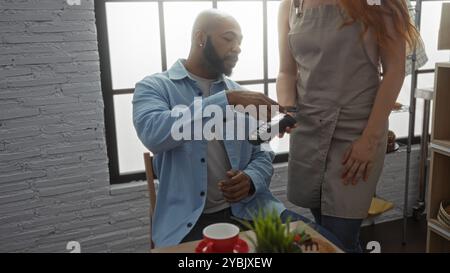 Mann, der mit Karte bezahlt, als Kellnerin hält Kartenleser im modernen Bäckereiinnenraum Stockfoto