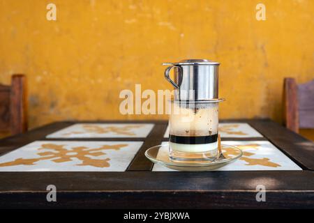 Ein Glas traditioneller heißer vietnamesischer Kaffee mit Kondensmilch auf einem Holztisch im Café in Vietnam. Stockfoto