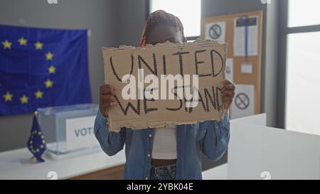Afrikanische Frau, die ein Schild mit der Aufschrift "united we stehen" vor der Flagge der europäischen union im Wahlraum hält Stockfoto