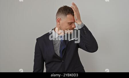 Ein junger Mann in einem Anzug erscheint vor weißem Hintergrund gestresst und zeigt einen universellen Ausdruck von Sorge oder Irrtum. Stockfoto