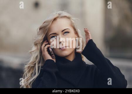 Die junge Frau hält ihr Telefon an ihr Ohr, während sie ihr Haar aus den Augen drückt, mit einem frustrierten Gesichtsausdruck Stockfoto