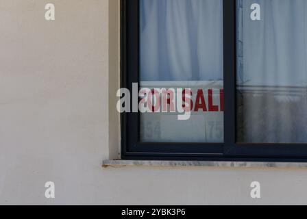 Ein hellrotes Schild zum Verkauf ist durch ein Fenster zu sehen, das auf die Möglichkeit einer neuen Residenz in einer ruhigen Nachbarschaft bei Tageslicht hinweist. Stockfoto