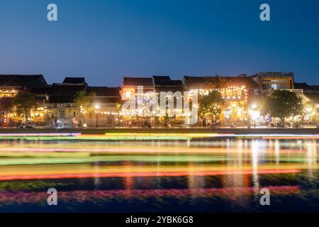 Leichte Spuren von Booten mit traditionellen Laternen auf der Fahrt. Nächtliche Szene des Wasserkanals und der Uferpromenade in der antiken Stadt Hoi an in Vietnam. Stockfoto