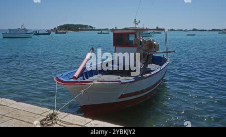 Das Fischerboot legte im klaren blauen Wasser von porto cesareo, italien, an, mit anderen Booten und einer Insel im Hintergrund unter einem hellen sonnigen Himmel. Stockfoto