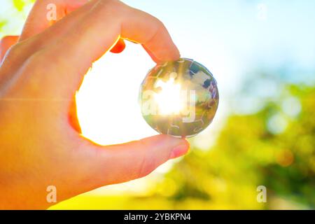 Konzept der erneuerbaren Energie mit einer Hand, die ein kugelförmiges Puzzleteil hält, beleuchtet durch Sonnenlicht. Stockfoto