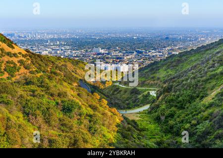 Atemberaubende Luftperspektive vom Runyon Canyon aus mit üppigen Hügeln, gewundenen Pfaden und weitläufiger urbaner Landschaft von Los Angeles in der Ferne. Stockfoto