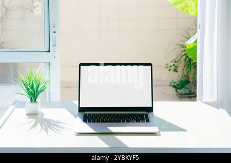 Laptop auf einem Schreibtisch mit weißem Bildschirm zum Mockup. Es sind keine Leute am Tatort. Computer neben dem Fenster. Sammlung von Fotos mit klarem, hellem Farbton Stockfoto