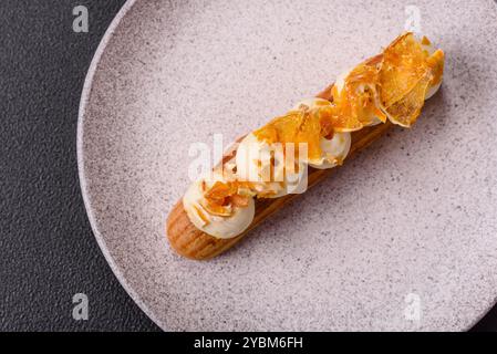 Süße Desserteclairs oder Profiterolen mit Schokoladenfüllung, bedeckt mit Sahne und getrockneten Orangen auf dunklem Betonhintergrund Stockfoto