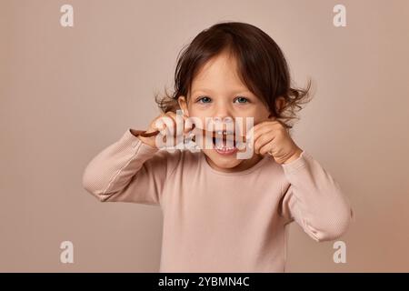 Niedliches Kindermädchen beißt Fruchtpastille auf beigefarbenem Hintergrund. Gesunde Babynahrung. Stockfoto