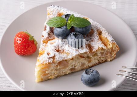 Köstliches Stück Kuchen mit frischen Heidelbeeren und einer Erdbeere auf einem hellen Holztisch Stockfoto