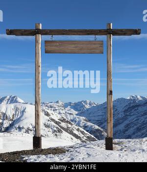 Holztor mit einem leeren Schild auf einem schneebedeckten Berg. Modell zum Hinzufügen von Roadmap-Text Stockfoto