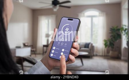 Steuerung des Deckenventilators im Wohnzimmer mit einer mobilen App. Frauenhand hält Smartphone, passt Lüftereinstellungen an, moderne Smart-Home-Technologie für Stockfoto