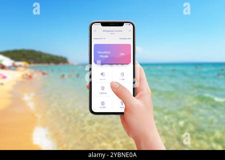 Steuerung von Kühlschrank und Küchengeräten vom Strand aus mit aktiviertem Urlaubsmodus. Mobile App in der Hand, genießen Sie den Komfort Ihres Smart Home und entspannen Sie sich Stockfoto