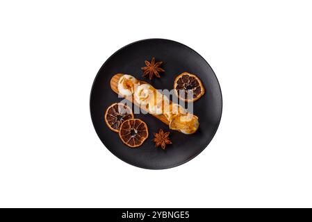 Süße Desserteclairs oder Profiterolen mit Schokoladenfüllung, bedeckt mit Sahne und getrockneten Orangen auf weißem Hintergrund Stockfoto