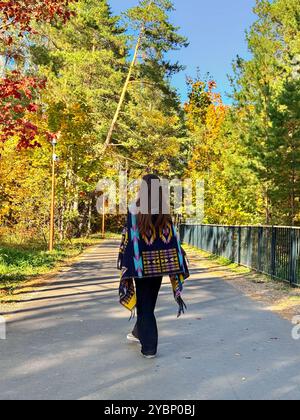 Eine junge Frau mit langen Haaren in einem Poncho läuft die Straße im Wald entlang, Blick nach hinten. Atmosphärisches Foto am Telefon einer Frau, die im Wald läuft Stockfoto
