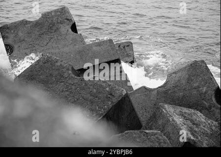 Schwarz-weiß-Bild von geometrischen Betonblöcken an der Seixal-Küste, die als Wellenbrecher gegen die Wellen des Atlantischen Ozeans entworfen wurden Stockfoto