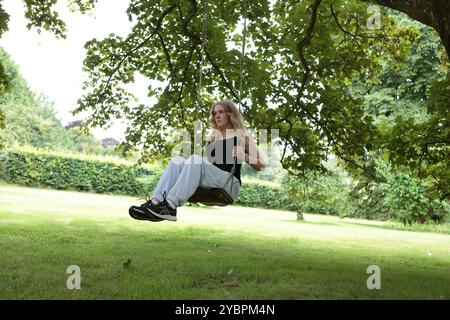 Teenager-Mädchen auf Schaukel unter Baum im Garten im Sommer Stockfoto