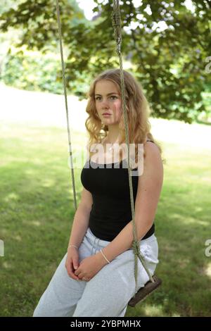 Teenager-Mädchen auf Schaukel unter Baum im Garten im Sommer Stockfoto