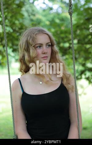 Teenager-Mädchen auf Schaukel unter Baum im Garten im Sommer Stockfoto