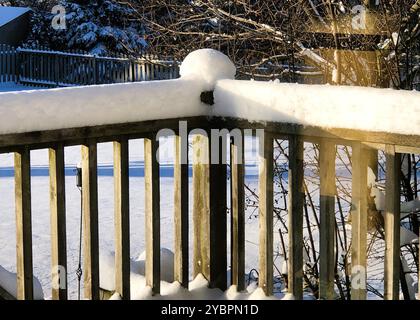 Am späten Nachmittag wirft die Sonne lange Schatten auf den frischen, weißen Schnee, der sich zu Beginn des Winters auf den Geländern und Pfosten eines Hinterhofdecks aufbaut. Stockfoto