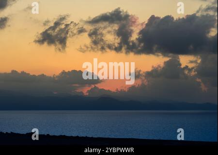 Ein atemberaubender Sonnenuntergang entfaltet sich, während der Himmel die Farben Orange und Rosa wechselt und ein ruhiges Leuchten über dem ruhigen Ozean ausstrahlt, umgeben von sanften Wolken. Stockfoto