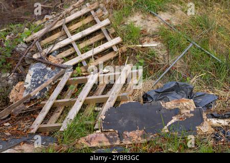 Gebrochene Holzpalette und Ablagerungen, die auf dem Boden in einem vernachlässigten Außenbereich verstreut waren. Das Konzept der Umweltverschmutzung und der entsorgten Stoffe Stockfoto