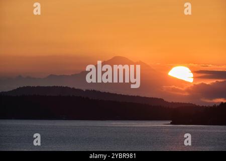 Durch einen Morgennebel, mit einem wunderschönen orangen Himmel, sieht man die Sonne aufgehen neben dem Mt. Baker von Arbutus Ridge auf Vancouver Island 130 km A. Stockfoto