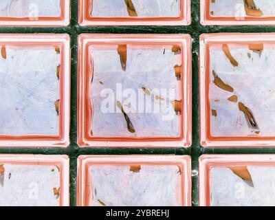 Transparente, rosafarbene Glaswand. Dekorativer Block aus Ziegelstein- und Glasquadraten. Moderne Inneneinrichtung für die Dusche. Abstrakter nahtloser Hintergrund. Stockfoto