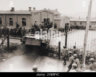 Alliierte Kriegsgefangene, die in einem Lager in der Nähe von Hammelburg inhaftiert sind, jubeln, als ein amerikanischer Panzer durch das Stacheldrahtzauge des Gefängnislagers abstürzt. Stockfoto