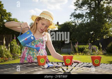 Vorjugendliches kaukasisches Mädchen, das Blumentöpfe in einem Garten tränkt Themen der wartenden Ungeduld Gärtner Pflege Stockfoto