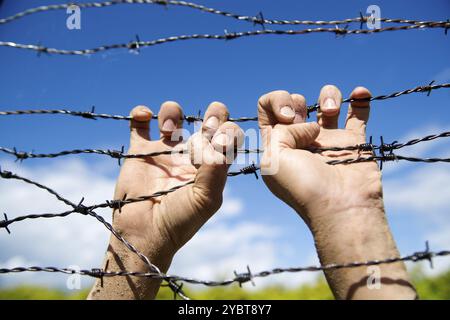 Hände greifen der Stacheldraht im Zeichen weg mit dem blauen Himmel Hintergrund ausgeführt Stockfoto